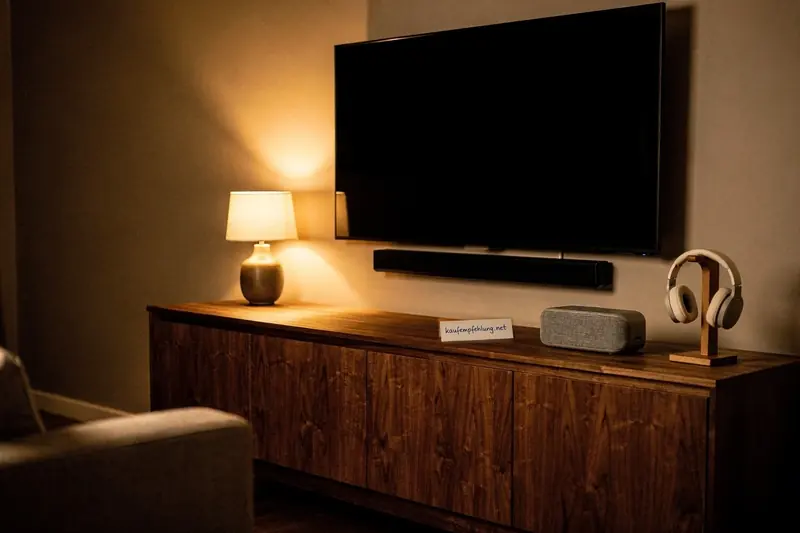 Wohnzimmer-Sideboard am Abend mit Fernseher, Soundbar, Bluetooth-Lautsprecher und Kopfhörern auf Ständer