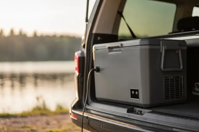 Graue Kompressor-Kühlbox mit Anschlusskabel im Kofferraum eines Campers am See