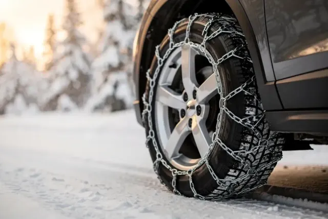 Montierte Schneekette aus Stahl auf einem Autoreifen im Schnee vor verschneitem Winterwald