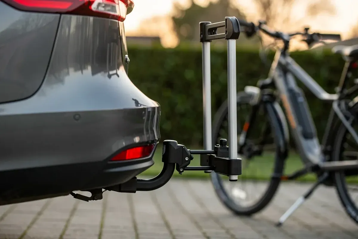 Zusammengeklappter Fahrradträger auf der Anhängerkupplung eines Autos, daneben zwei E-Bikes in der Einfahrt