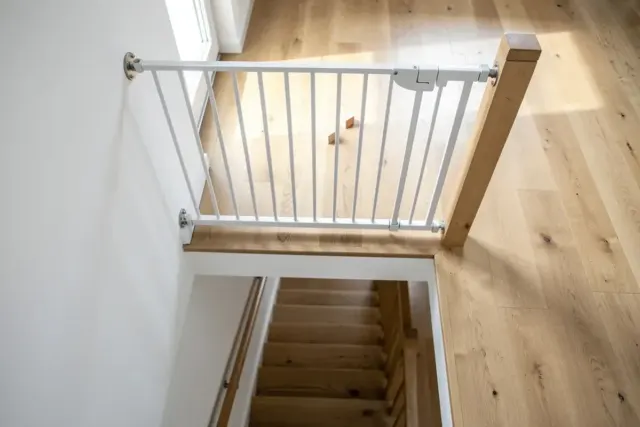 Weißes Treppenschutzgitter, fest verschraubt am oberen Ende einer Holztreppe, Blick von oben