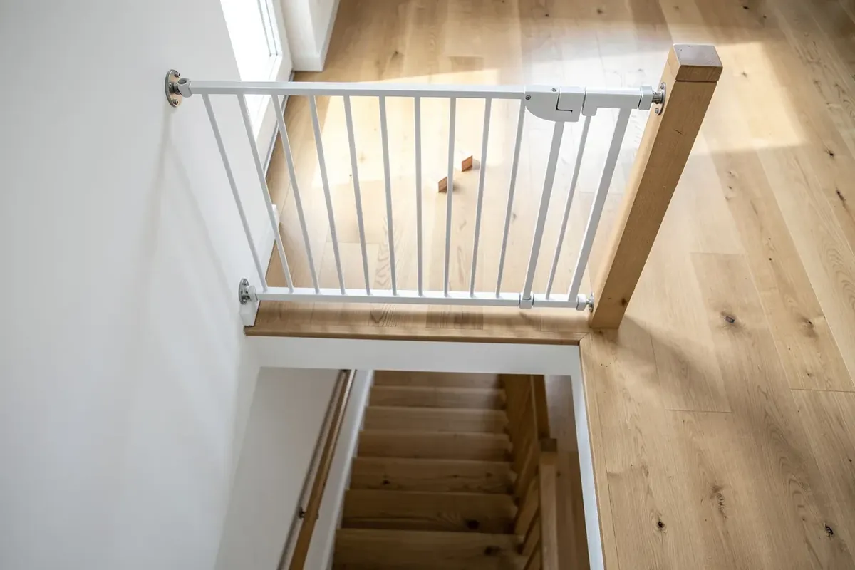 Weißes Treppenschutzgitter, fest verschraubt am oberen Ende einer Holztreppe, Blick von oben