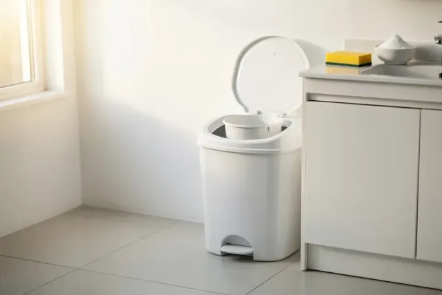 Geöffneter weißer Windeleimer im hellen Bad, daneben Schwamm und Schale mit Natron auf dem Waschtisch